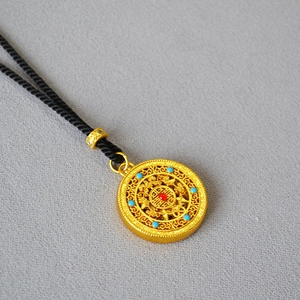 Detail of filigree gold-plated pendant with red and blue beads on black woven cord