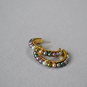 Detail of C-shaped gold earrings with colorful pearls in vintage French design