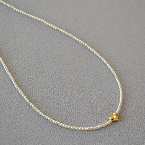 Elegant pearl necklace featuring a minimalist gold heart pendant on grey fabric