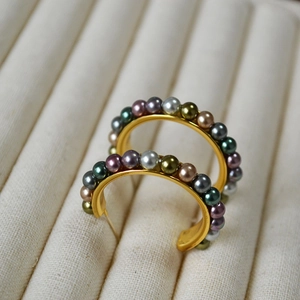 Close-up of C-shaped gold hoop earrings with multi-colored pearls on a jewelry tray