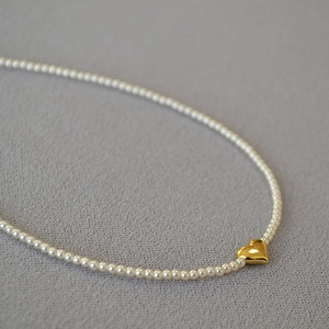 Close-up of elegant small pearl necklace featuring a polished gold heart pendant