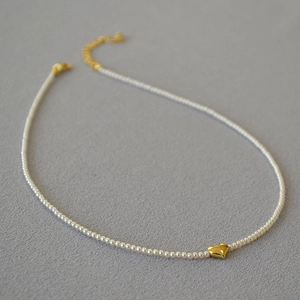Close-up of minimalist pearl necklace featuring a polished gold heart pendant on grey texture