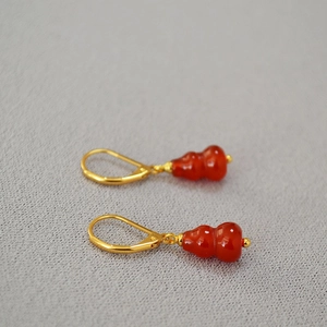 Detailed view of red agate gourd earrings with gold hooks on a textured background