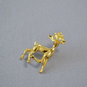 Makroaufnahme einer goldenen Elch-Brosche mit Schneeflocken-Geweih auf grauem Stoff