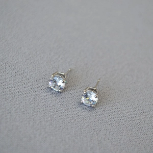 Detailed top view of four-prong round zircon earrings on a grey textured background