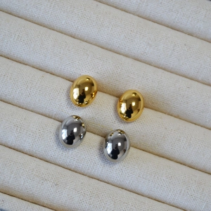Macro detail of polished oval bean stud earrings in gold and silver finish on fabric