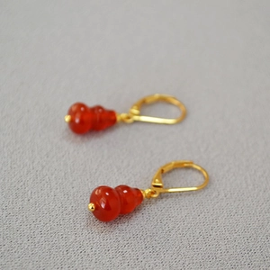 Macro view of Chinese style gold gourd earrings featuring red agate stone drops