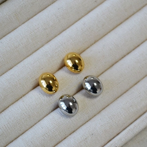 Detailed view of polished oval gold and silver stud earrings on a beige display tray