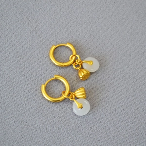Détail du pendentif lotus doré et de la boucle d'oreille en jade blanc sur fond gris