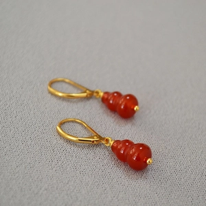 Chinese style red agate gourd earrings with gold hooks on a textured grey surface