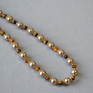 Detailed close-up of tiger eye stones and champagne pearls with golden spacers on a necklace