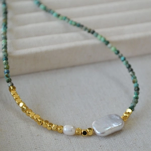 Macro shot of turquoise stone beads with a large baroque pearl on beige fabric