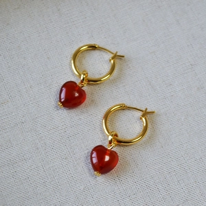 Elegant gold hoop earrings with red heart-shaped agate pendants on white fabric
