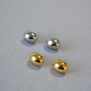Macro shot of minimalist gold and silver oval pebble earrings with high-polish mirror finish