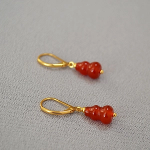 Macro shot of French hook earrings with red agate stones in a golden gourd shape