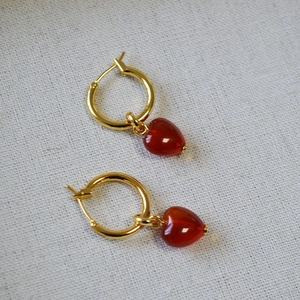 Detail of gold hoop earrings featuring vibrant red heart-shaped agate pendants on fabric