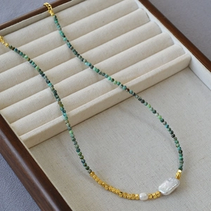 Detail of baroque pearl charms and turquoise beads on a gold necklace display