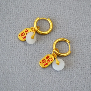 Détail de boucles d'oreilles dorées avec jade blanc et pendentif porte-bonheur