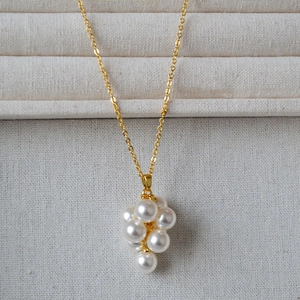 Collier élégant doré avec pendentif grappe de perles brillantes sur fond texturé raffiné