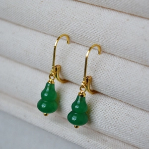 Macro shot of gold hook earrings with green agate gourd pendants in a jewelry box