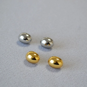 Macro shot of oval gold and silver studs with high-polish finish on grey fabric