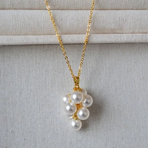 Gros plan d'un collier doré avec un pendentif grappe de perles blanches délicates sur tissu