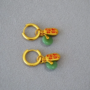 Détail de boucles d'oreilles dorées avec perles de jade vert et charmes rouges