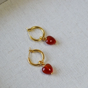 Detailed view of gold hoop earrings with polished red agate heart-shaped pendants