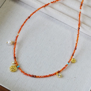 Detail of red carnelian beads, baroque pearl, and gold coin pendant on jewelry box