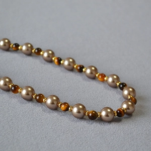 Macro detail of retro tiger eye stone and brown pearl beaded necklace with gold spacers