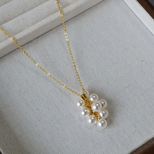 Détail d'un pendentif en perles en forme de grappe sur une fine chaîne dorée et lin fin