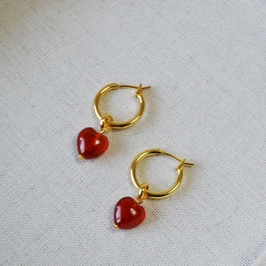 Elegant gold hoop earrings featuring red heart-shaped pendants for a minimalist style