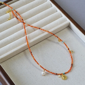 Detailed shot of red beaded necklace featuring gold coin pendant and freshwater pearls