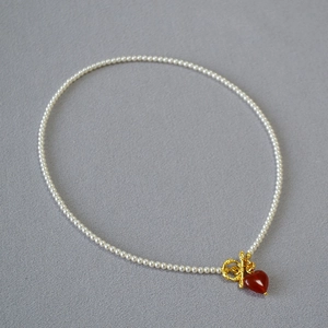 Detail of pearl necklace with gold OT clasp and a red heart-shaped agate pendant