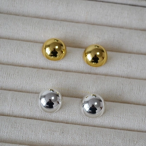 Macro detail of polished gold and silver ball stud earrings on a beige velvet jewelry tray