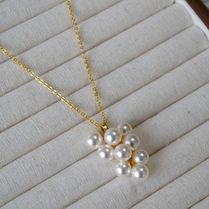 Gros plan sur le collier à pendentif perles en grappe dorée sur velours beige