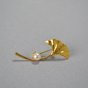 Detailed macro view of gold ginkgo leaf brooch featuring a white pearl and vein texture