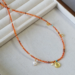 Detail of red beaded necklace with gold coin pendant and freshwater pearl on tray