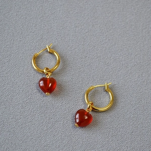Detailed close-up of golden hoop earrings featuring translucent red heart-shaped pendants