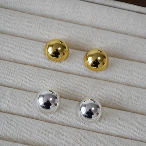 Close-up of polished gold and silver dome earrings set in a beige jewelry tray
