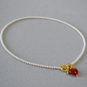 Close-up of pearl necklace featuring a red heart pendant with a vintage OT buckle