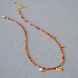 Detail of red beaded necklace with pearl pendant and golden coin charm on fabric