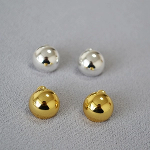 Macro view of gold and silver polished metal ball earrings on grey textured fabric