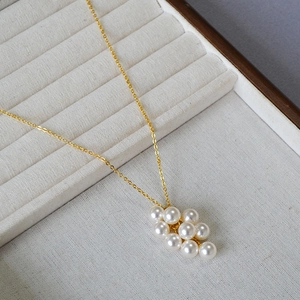 Détail macro d'un collier pendentif raisin en perles dorées dans son écrin beige