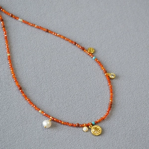 Close-up of red beaded necklace with freshwater pearl and gold coin pendant detail