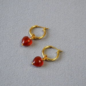 Detailed macro view of golden metal hoops with polished red heart-shaped agate pendants