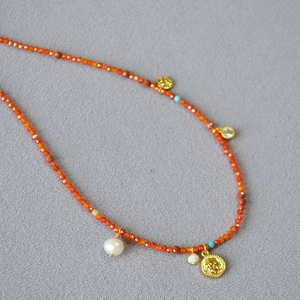 Detail of red beaded necklace featuring vintage gold coin pendant and baroque pearl