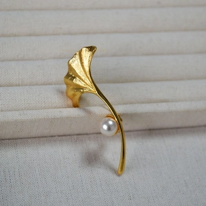 Macro detail of brushed gold ginkgo leaf brooch featuring a lustrous white pearl accent