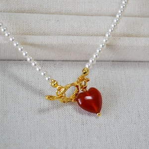 Detail of elegant pearl necklace featuring a red heart agate pendant and gold OT clasp