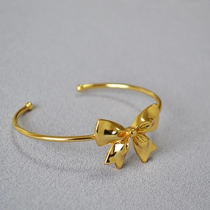 Polished gold-plated brass open cuff bracelet with minimalist bow design on fabric back